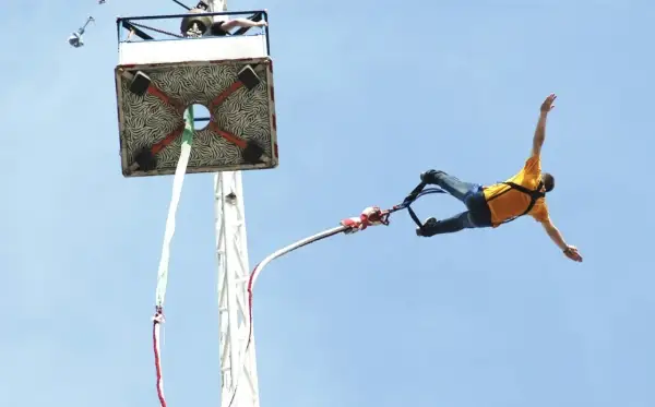 Odwaga w czystej postaci: mężczyzna w żółtej koszulce wykonuje ekscytujący skok na bungee, szybując w błękitnym niebie.