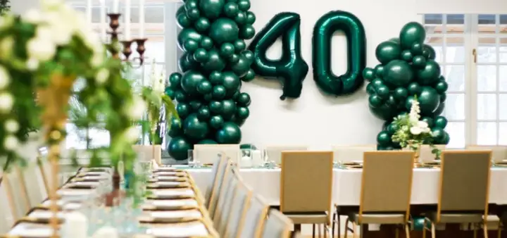Uroczyste przyjęcie z okazji wyjazdu na 40 urodziny. Zielone balony tworzą łuki i liczbę 40, a stół jest nakryty na elegancką kolację.
